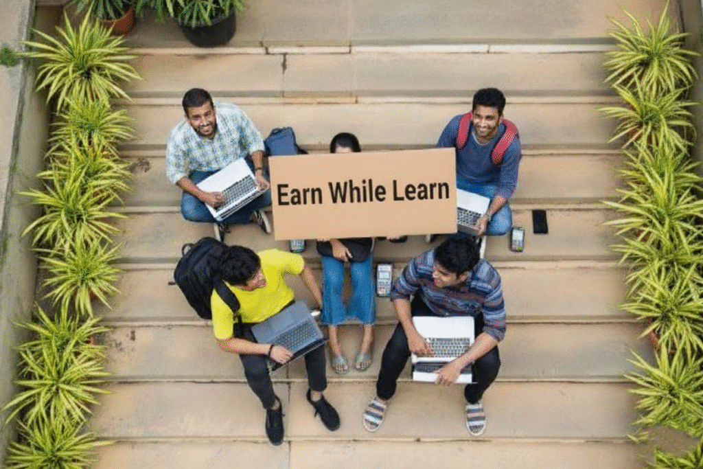 Four happy students sitting on steps with laptops, surrounding a sign that reads "Earn While Learn," symbolizing the financial freedom and work experience gained through the ISMT Earn-N-Learn MBA program.